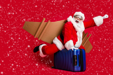 Full body size photo of retired infantile grandpa white beard ride suitcase jetpack play hero save universe wear santa x-mas costume coat spectacles headwear isolated red color background