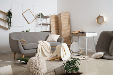 Interior of messy living room with sofa, overturned table and broken things after earthquake