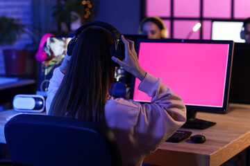 Young woman with headphones playing computer game in club at night, back view