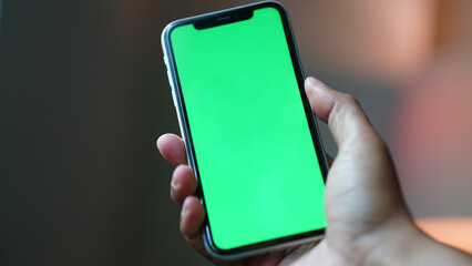 Hand holding smartphone with green screen display. Focus selected