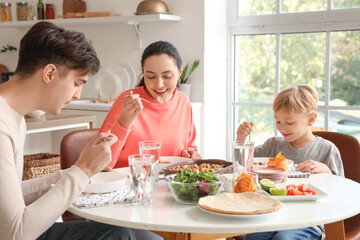 Little boy with his parents eating Fajita at table in kitchen
