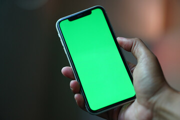 Hand holding smartphone with green screen display. Focus selected