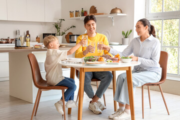 Little boy and his parents with glasses of water eating Fajita at table in kitchen