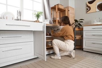 Young woman taking utensil from open drawer in kitchen