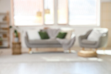 Blurred view of light living room with grey sofa, armchair and window