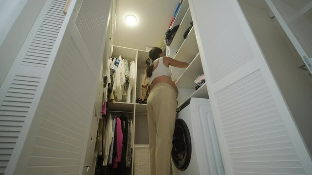 A pregnant woman standing near a mirror at home, putting on clothes. The scene reflects self-care, maternity, and everyday life in a warm and personal setting