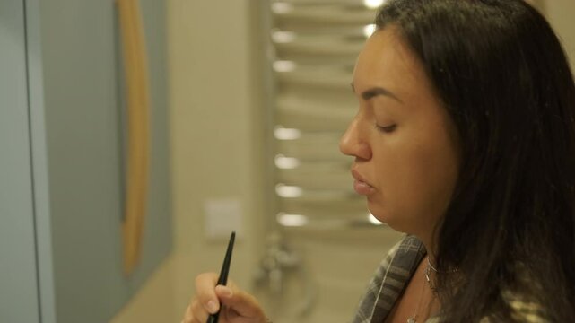 A pregnant woman standing near a mirror at home, putting on clothes. The scene reflects self-care, maternity, and everyday life in a warm and personal setting