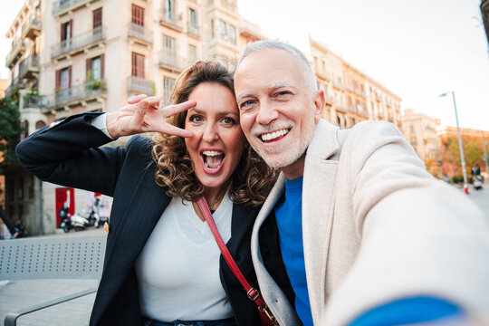 Happy mature couple taking selfie and making peace sign while enjoying autumn day in Barcelona. Middle aged people showing genuine joy and connection and having fun during their vacations