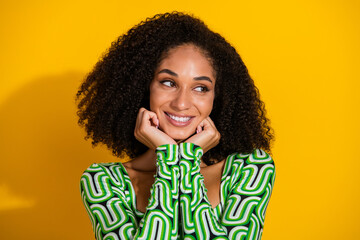 Charming young woman with curly hair against vibrant yellow background, wearing a stylish green top, exuding happiness and confidence