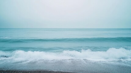 A hazy, muted seascape with gentle waves crashing on a pebbled shore.