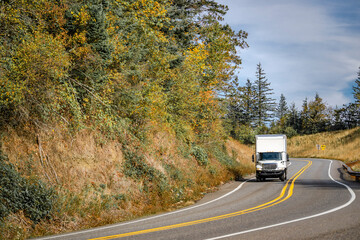 Local carrier middle duty day cab white rig semi truck transporting cargo in box trailer driving on...