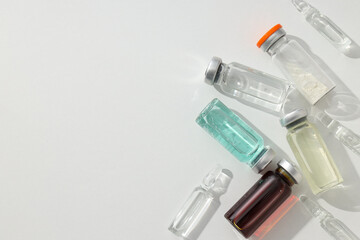 Glass medical bottles and ampoules with vaccine on white background, space for text