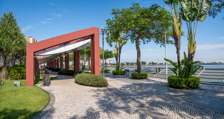 A peaceful waterfront park in Macao, China, featuring a covered pergola for rest, paved footpath,...