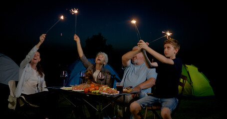 family with grandparents having fun and playing fire sparkle while camping in the outdoors  with smiles, laughter, and joy, celebrating together