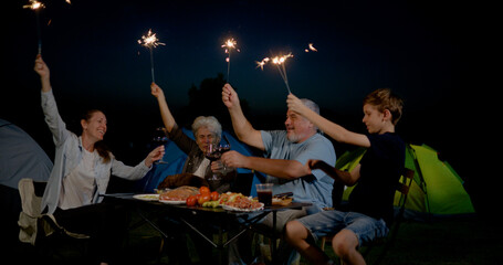 family with grandparents having fun and playing fire sparkle while camping in the outdoors  with smiles, laughter, and joy, celebrating together