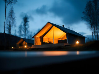Fototapeta premium A cozy tent cabin illuminated warmly at dusk, surrounded by trees under a cloudy sky, inviting tranquility and adventure in nature.