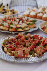 A silver platter with a variety of appetizers including meat, olives, and bread. The platter is set on a table with other platters of food