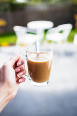 hand holding coffee in clear mug in front of blurred home interior background, habits and lifestyle concept