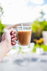 hand holding coffee in clear mug in front of blurred home interior background, habits and lifestyle concept
