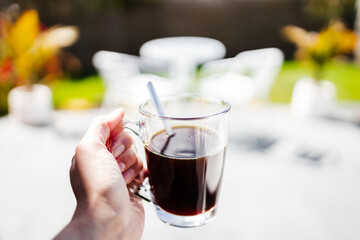 hand holding coffee in clear mug in front of blurred home interior background, habits and lifestyle concept