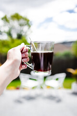 hand holding coffee in clear mug in front of blurred home interior background, habits and lifestyle concept