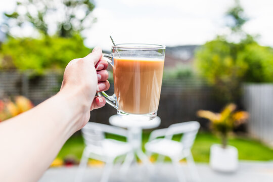 hand holding coffee in clear mug in front of blurred home interior background, habits and lifestyle concept
