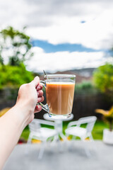 hand holding coffee in clear mug in front of blurred home interior background, habits and lifestyle concept