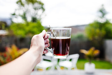 hand holding coffee in clear mug in front of blurred home interior background, habits and lifestyle concept