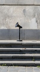 A black megaphone stands alone on stone steps against a textured wall.