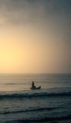 Fototapeta premium A lone fisherman rows his small boat towards the horizon, silhouetted against a stunning sunrise. A timeless scene of human resilience and connection with nature, perfect for travel, documentary, and 