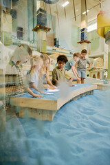 Cute little friends creating pictures on top of table with blue sand on spacious playground at leisure center