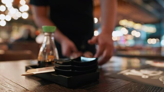 Blurred interior of large beautiful restaurant with bright lighting. Waitress comes to working bar bartender gives visitors brings customer's sushi order and places it on table. Food drink people
