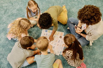 High angle of clever little boys pointing at letter of English alphabet while answering question of...