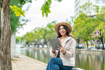 Fototapeta premium Asian female tourist using tablet for travel booking near Tha Phae Gate in Chiang Mai. Young woman planning itinerary or hotel arrangements while exploring city on vacation.