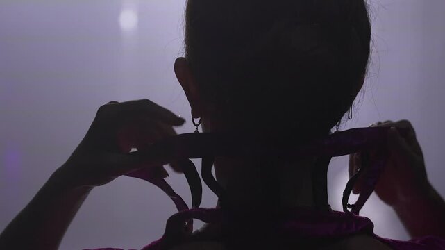 A young female artist adjusts her costumes collar backstage before stepping onto the stage, captured in a candid moment from behind. 