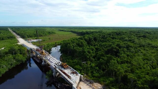 Construction site for a bridge over a calm river, surrounded by dense green forest and wetlands. Corozal, Belize.