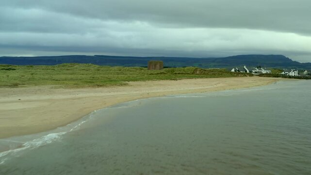 Low aerial dolly glides over water, sand, and dunes towards the Magilligan Martello Tower.
