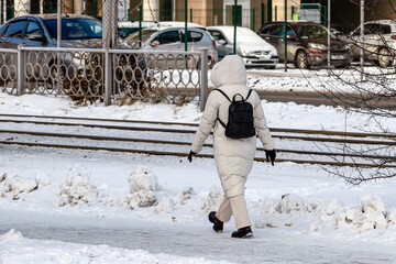 A woman with a backpack walks along a snow-covered sidewalk on a winter day