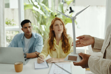 Engineer showing the work of windmill to colleagues while they sitting at table during presentation in office