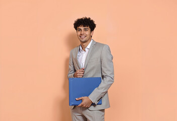 Portrait of a smiling young man in a grey suit holds a blue folder against a peach background