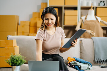 Young business owner woman prepare parcel box and standing check online orders for deliver to...