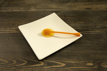 A plastic honey dipper or drizzler stick on top of a small white plate.