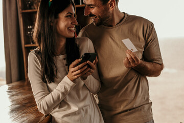 Happy couple using credit card and phone while buying online for Christmas at home.
