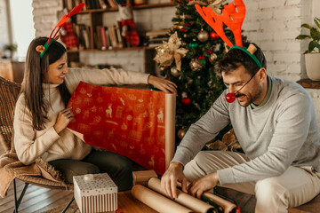 Mid aged couple wrapping Christmas gifts. They are wearing sweaters and having fun.