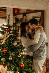 Image of a mid 30's couple decorating a Christmas tree in their living room. They are hugging while choosing baubles and ornaments and enjoying their holiday.