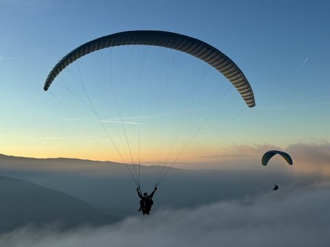 Parapente au dessus du Lac d' Annecy. Vol de parapente en montagne au dessus du brouillard. Sport extr&ecirc;me. Voler le soir au dessus de la brume avec un coucher de soleil.