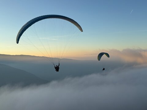 Parapente au dessus du Lac d' Annecy. Vol de parapente en montagne au dessus du brouillard. Sport extr&ecirc;me. Voler le soir au dessus de la brume avec un coucher de soleil.