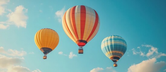 Obraz premium Three colorful hot air balloons fly in the sky, with fluffy white clouds in the background.