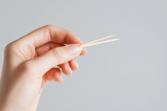 A hand holding two wooden toothpicks against a light background.