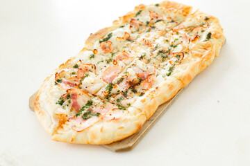 Pizza with bacon in Roman style served with fresh tomatoes on white table at cozy home